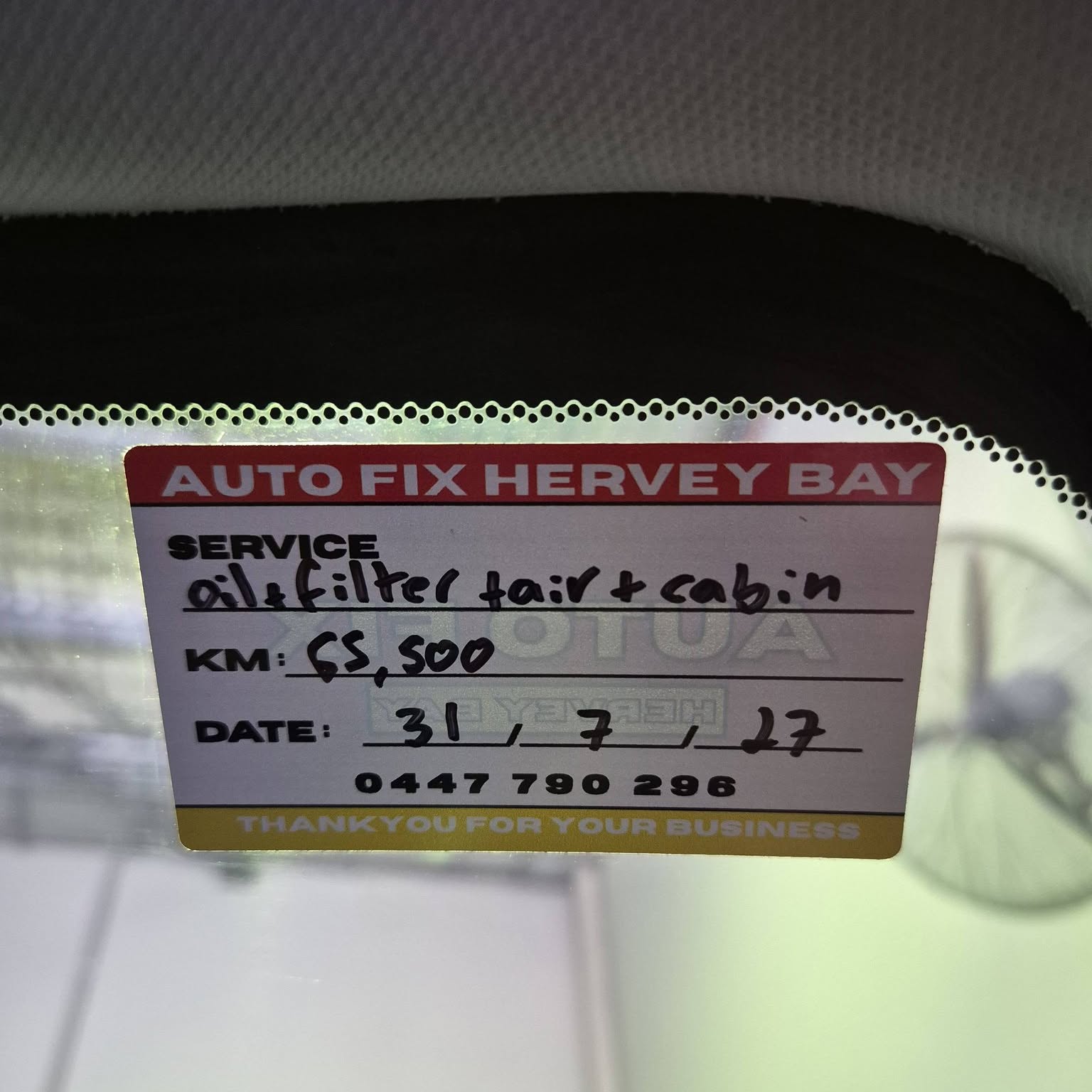 An Autofix Hervey Bay service reminder sticker on a windscreen, filled in by hand
