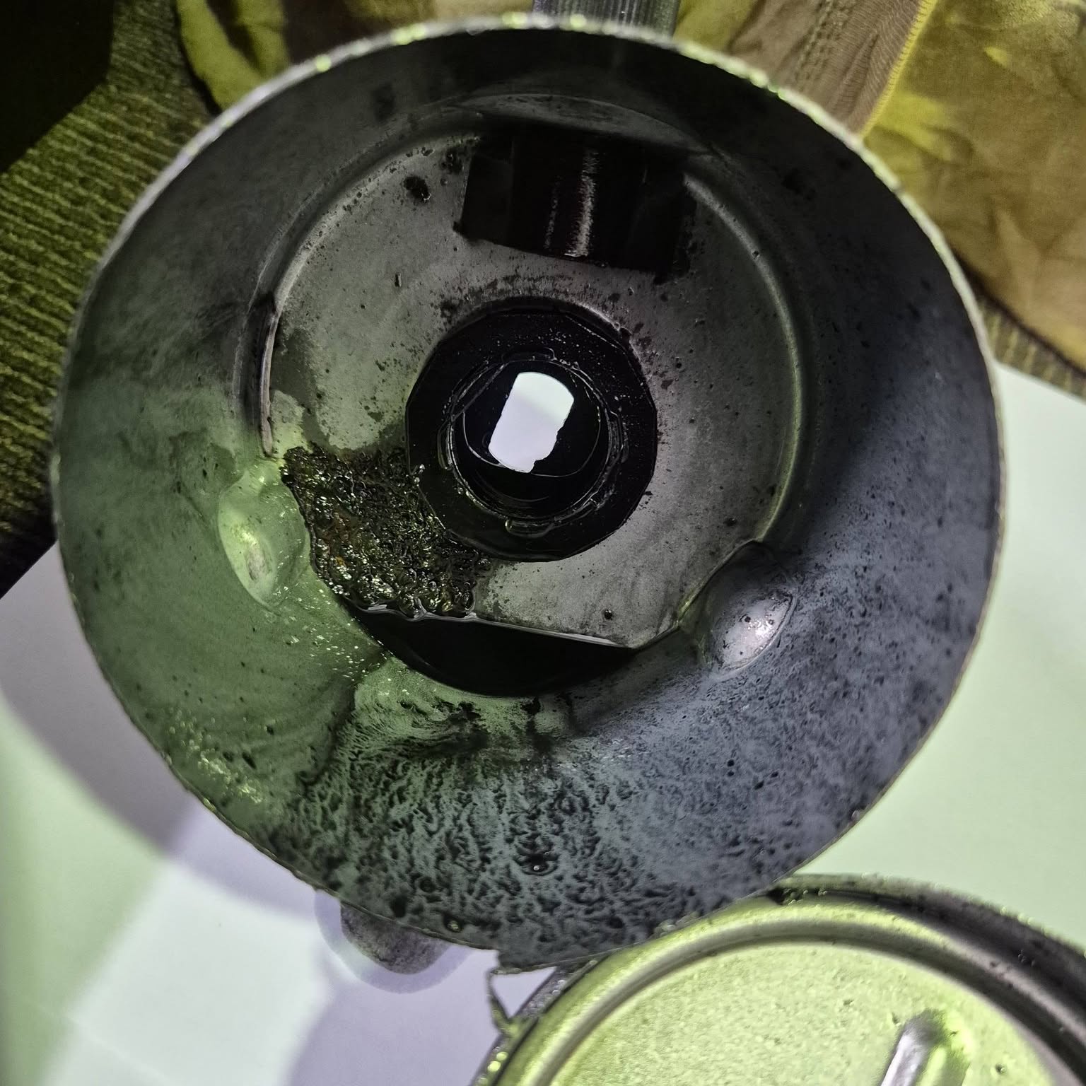 An oil filter housing cap coated in dirty oil, held in a gloved hand